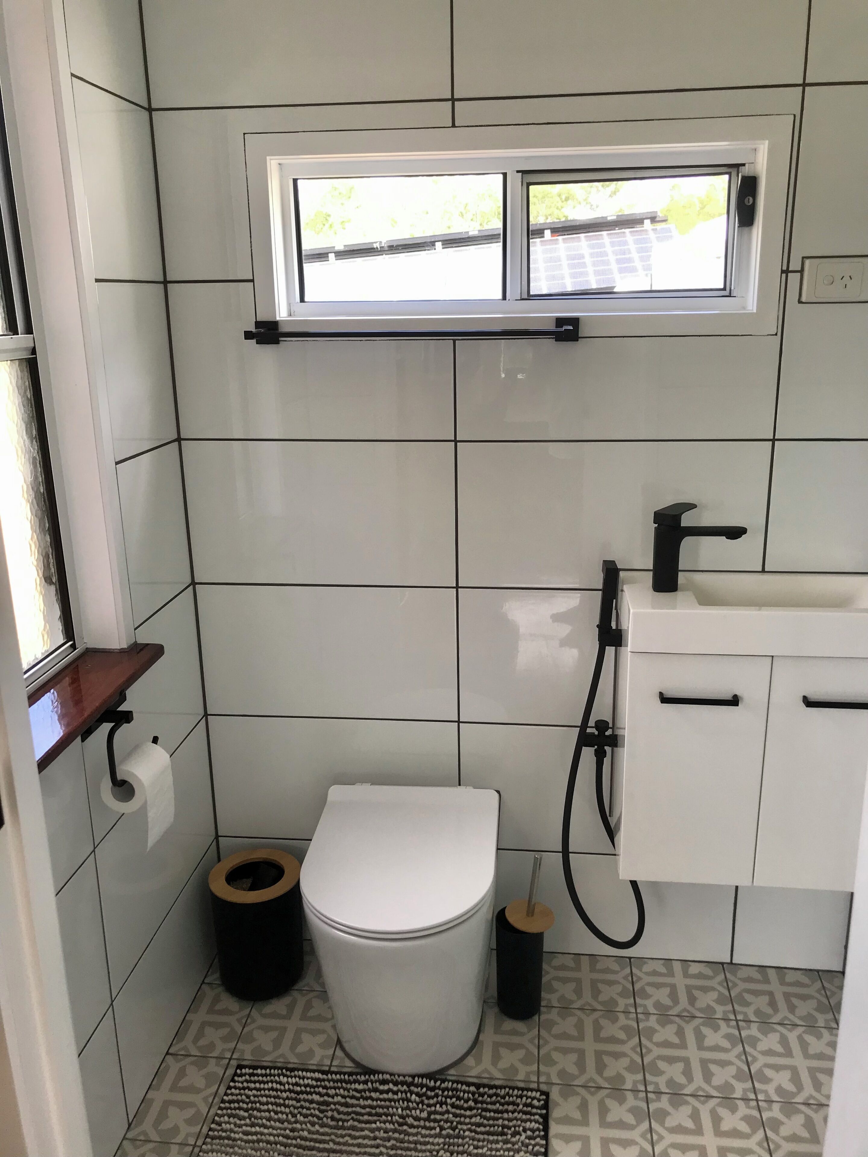 A small bathroom with a toilet, a sink, a window, and a toilet paper holder.