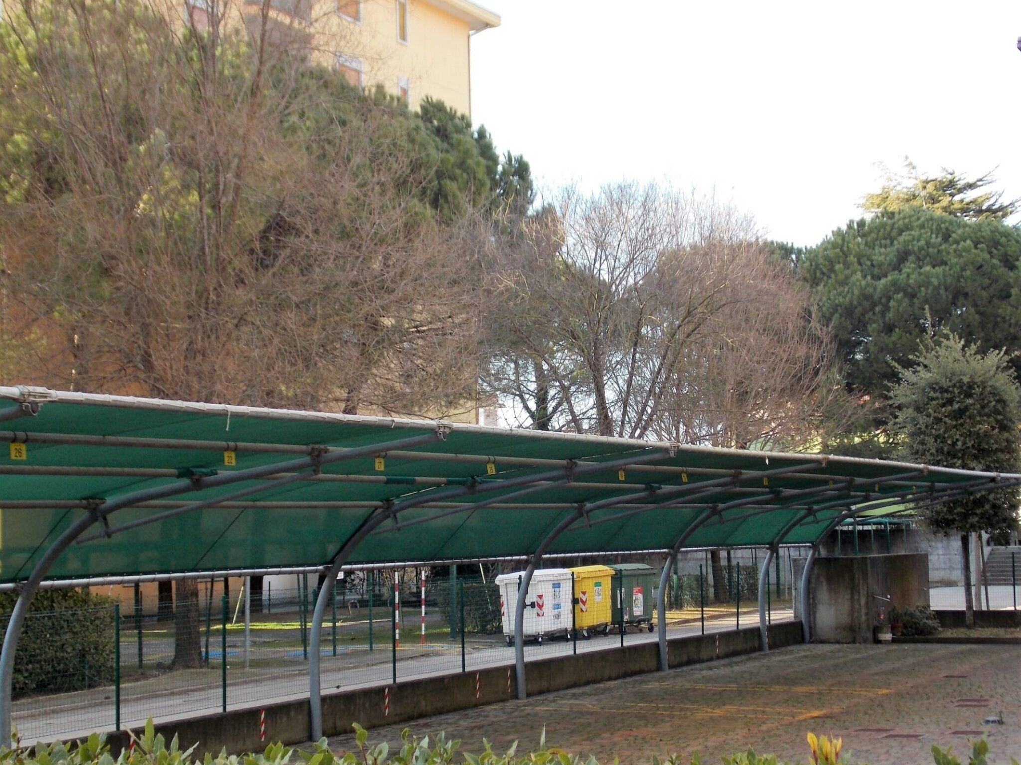 A covered outdoor area with a green roof, a fence, and a building in the background.