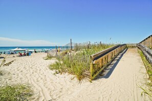 Ein sandiger Strand mit einer Holzpromenade, Strandstühlen und einem klaren, blauen Himmel.