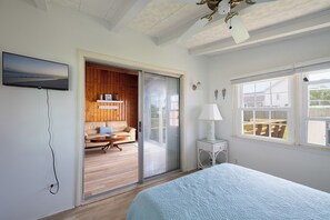 Ein Schlafzimmer mit Bett, Fernseher, einer Schiebetür zu einem Wohnbereich und einem Fenster mit Blick.