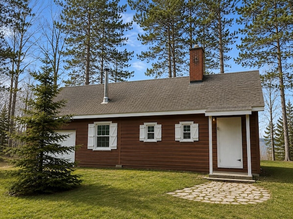 Une petite maison en bois d’un seul étage, avec une cheminée, des volets blancs et une porte d’entrée.