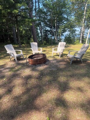 Een camping met vier Adirondack stoelen rond een vuurkuil.