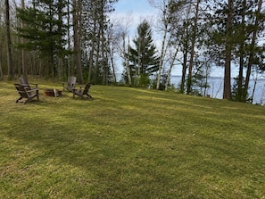 A grassy outdoor area with Adirondack chairs and a fire pit.