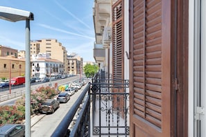 Un balcone con ringhiera in metallo che si affaccia su una strada con auto parcheggiate e edifici.