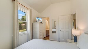 Ein Schlafzimmer mit Bett, Fernseher auf einem Schrank, Kleiderschrank, Bad und Nachttisch mit Lampe.