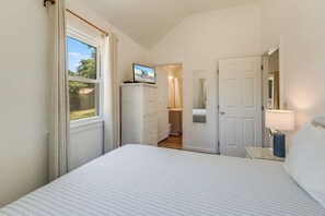 Ein Schlafzimmer mit Bett, Fernseher auf einem Schrank, Kleiderschrank, Bad und Nachttisch mit Lampe.