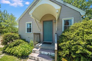 Ein eingeschossiges Haus mit Veranda, einer grünen Tür und einem kleinen Fenster auf der rechten Seite.
