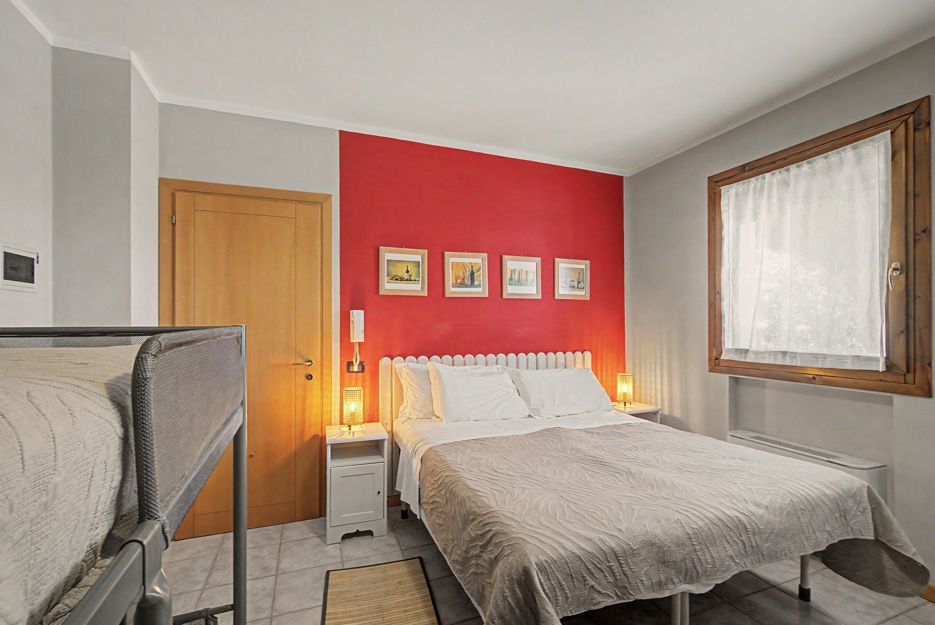 Een slaapkamer met een bed, nachtkastje, raam met gordijnen en een deur.
