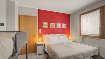 Een slaapkamer met een bed, nachtkastje, raam met gordijnen en een deur.