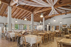 A spacious dining area with wooden tables and chairs, large windows, and a high wooden ceiling with exposed beams.