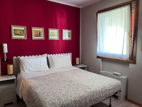 Una camera da letto con un letto, comodini, un telefono fissato al muro e quadri appesi.. Camera 'Papaveri E Papere - Cantina' con giardino in comune e Wi-Fi
