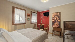 Ett hotellrum med en säng, en stol, ett litet bord, en tv och en tavla på väggen.