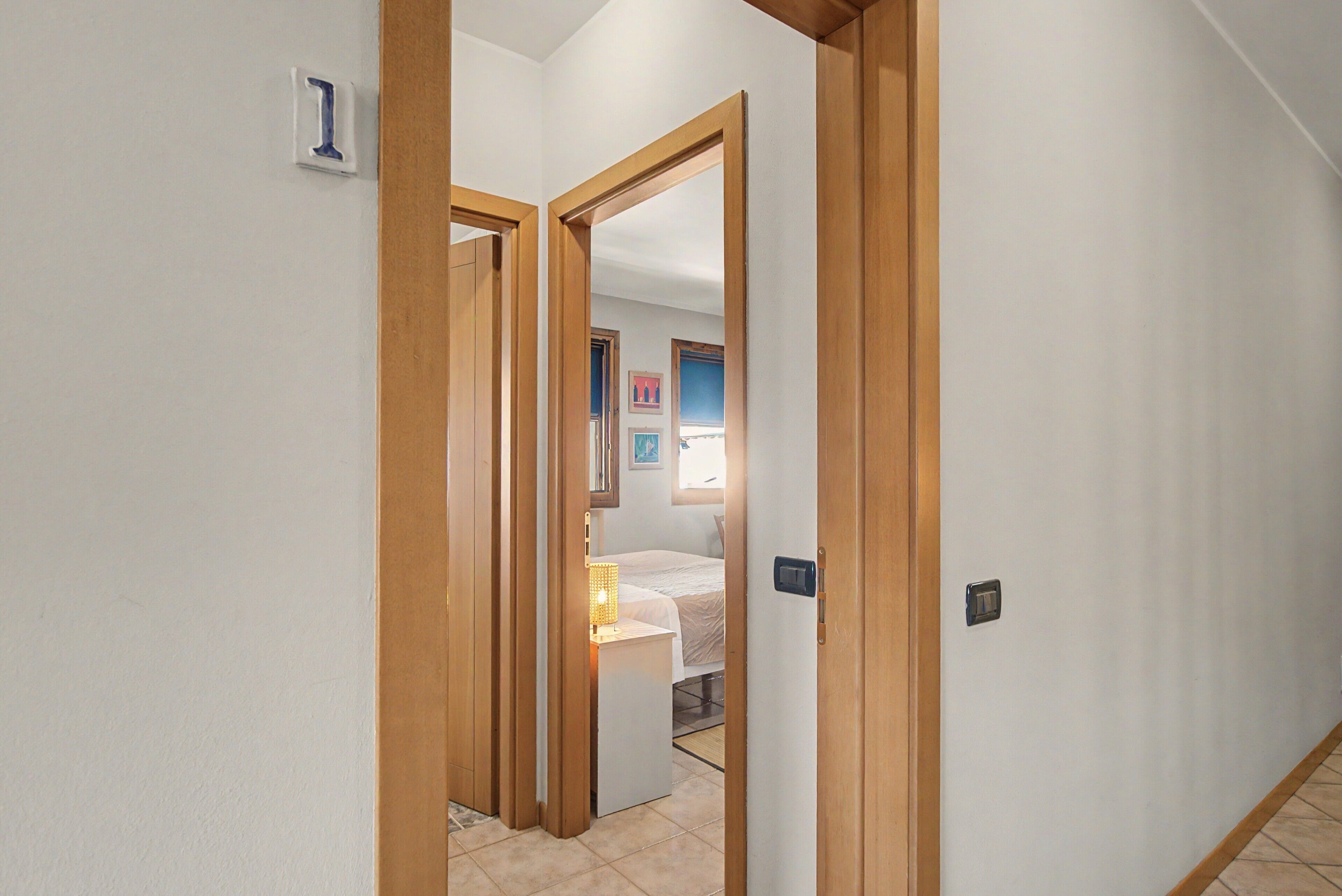 Ein Flur mit Holztüren, der zu einem Schlafzimmer mit einem Bett und einem Nachttisch führt.