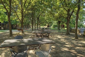 An outdoor seating area with tables and chairs, surrounded by trees.