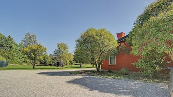 Een grindpad leidt naar een rood gebouw met een raam, omringd door bomen en een heldere lucht.