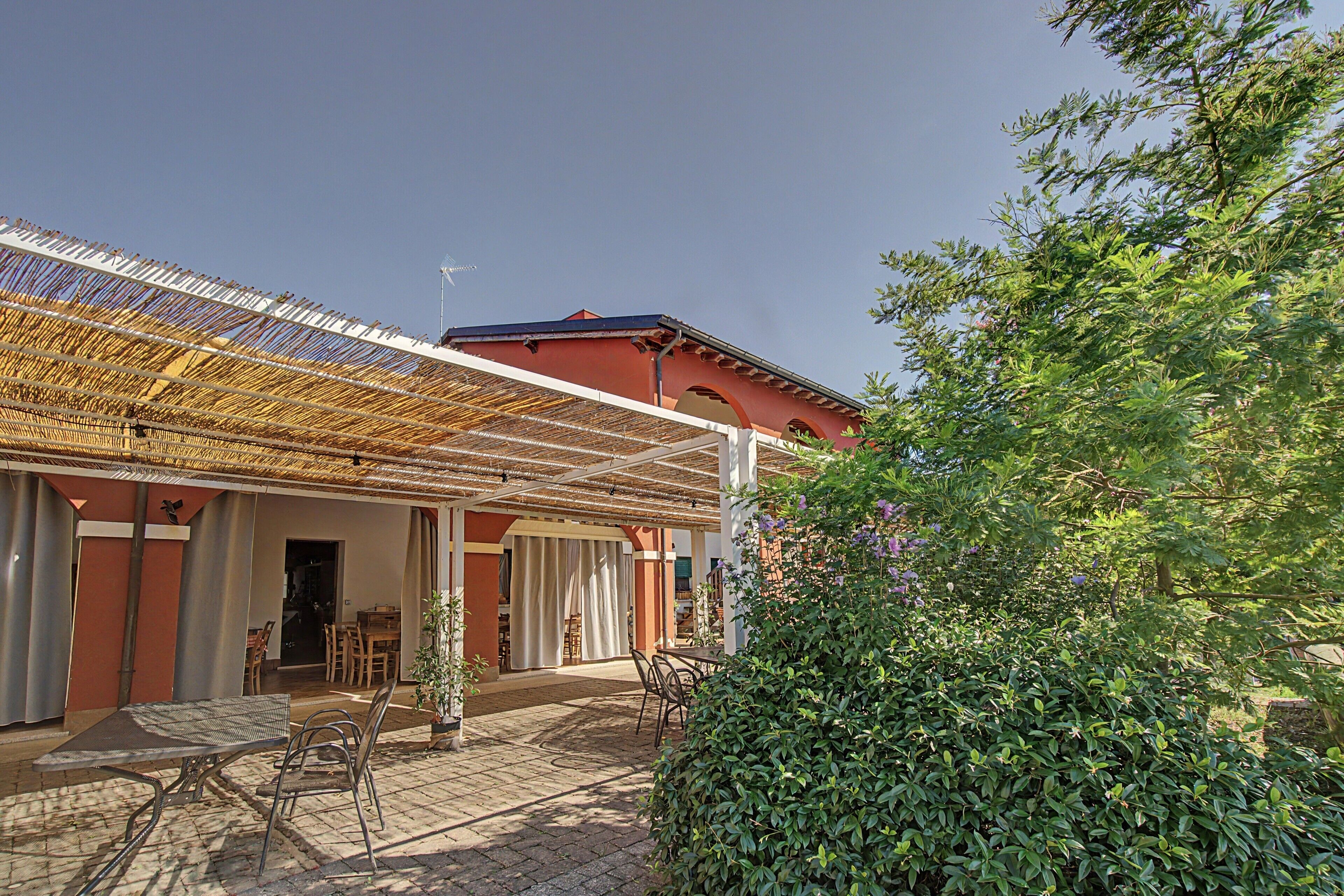 Un espace extérieur abrité, aménagé avec des tables et des chaises, un bâtiment à la façade rouge et un arbuste vert au premier plan.