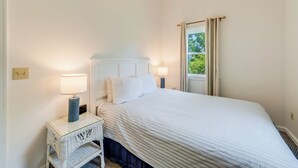 Ein Schlafzimmer mit einem Bett, Nachttischlampen, einem Beistelltisch und einem Fenster mit Vorhängen.