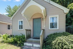 Einbungalow mit einer Veranda, einer grünen Tür und einem kleinen Vorgarten mit Pflanzen.