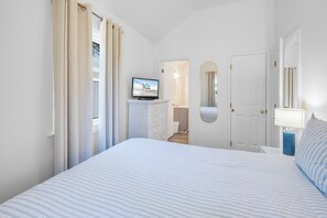Ein Schlafzimmer mit einem Bett, einem Fernseher auf einer Kommode, einer Tür und einem Spiegel.