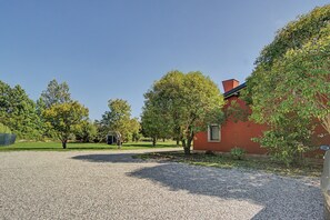 Soraa päällystetty ajotie johtaa punaiseen rakennukseen, jossa on ikkuna. Rakennuksen ympärillä on puita ja taivas on kirkas.