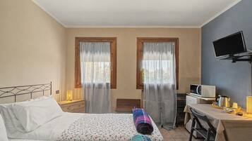 Ein Hotelzimmer mit einem Bett, einem Schreibtisch mit Computer, einem Fernseher und einem Fenster mit Vorhängen.