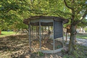 Ein Vogelhaus mit Drahtgitterdach und Holzunterlage, umgeben von Bäumen und Gras.