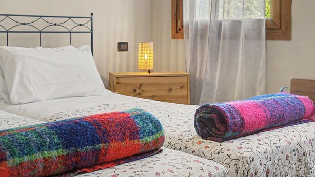 Een slaapkamer met een bed, nachtkastje, lamp en een raam met gordijnen.