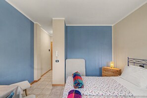 Ein Schlafzimmer mit einem Bett, einem Nachttisch mit Lampe, einem Sessel und einem an der Wand befestigten Telefon.