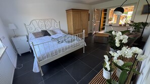 Ein Schlafzimmer mit einem Metallbettgestell, einem Holzschrank, einem Nachttisch mit Lampe und einer Orchideenpflanze im Topf.