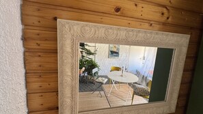 Ein gerahmter Spiegel, der einen Raum mit rundem Tisch, Stühlen und Zimmerpflanzen reflektiert.