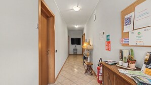 Ein Flur mit einer Holztür, einem Feuerlöscher, einem Schwarzebrett mit verschiedenen Bekanntmachungen und einem gefliesten Boden.