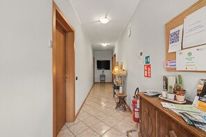 En hall med en dörr av trä, en brandsläckare, en anslagstavla med diverse meddelanden och ett klinkergolv.