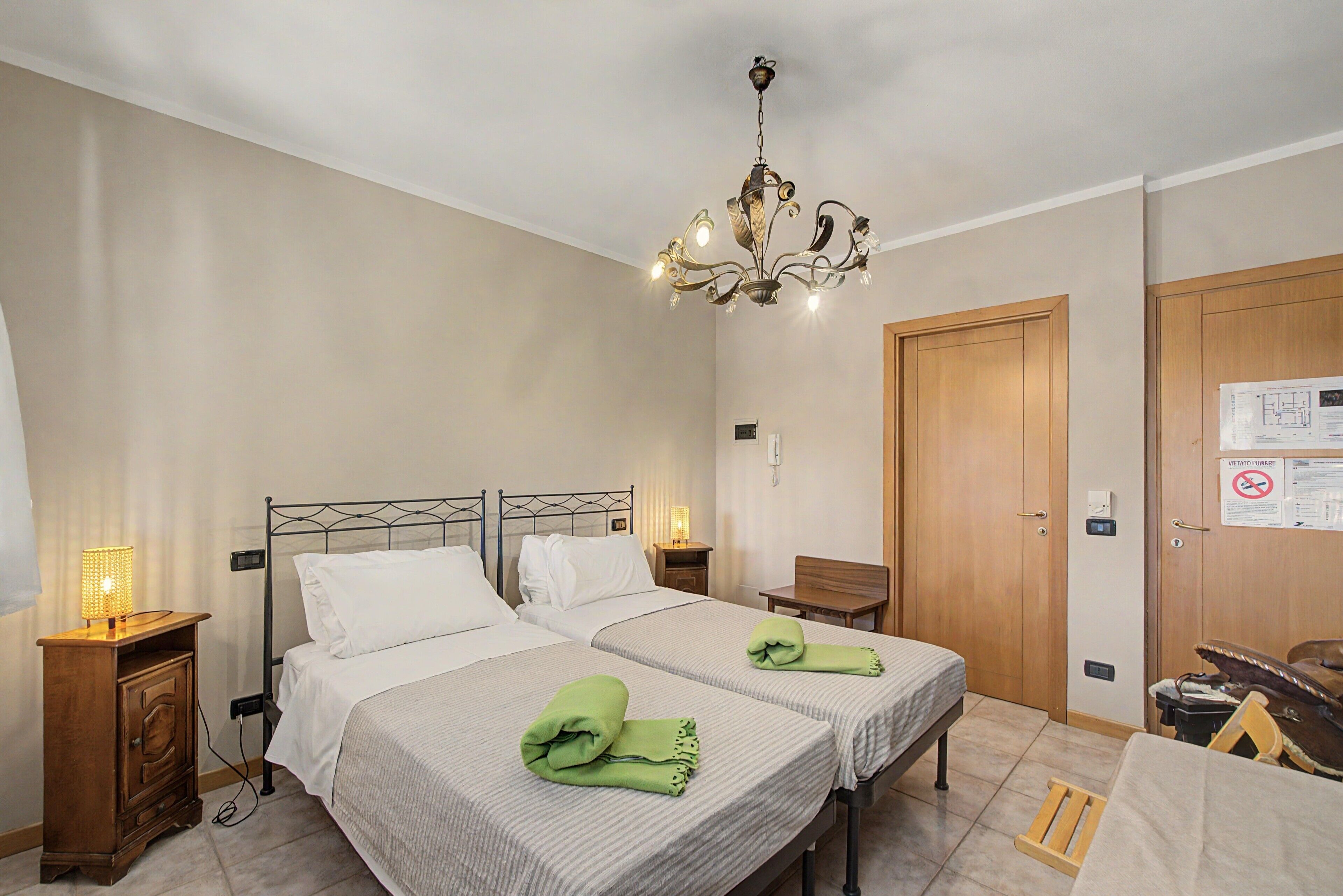 Ett hotellrum med två sängar, en kristallkrona, en garderob i trä och ett skrivbord med en stol.