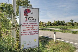 Ett vägskylt med text och logotyper, omgivet av grönska och en väg.
