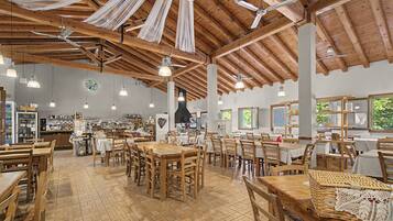 Un'ampia sala da pranzo con tavoli e sedie in legno, ventilatori a soffitto e lampade a sospensione.