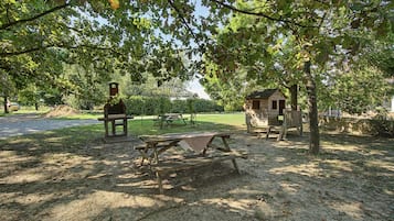 Zona de picnic con una parrilla, mesa y una pequeña estructura de madera.