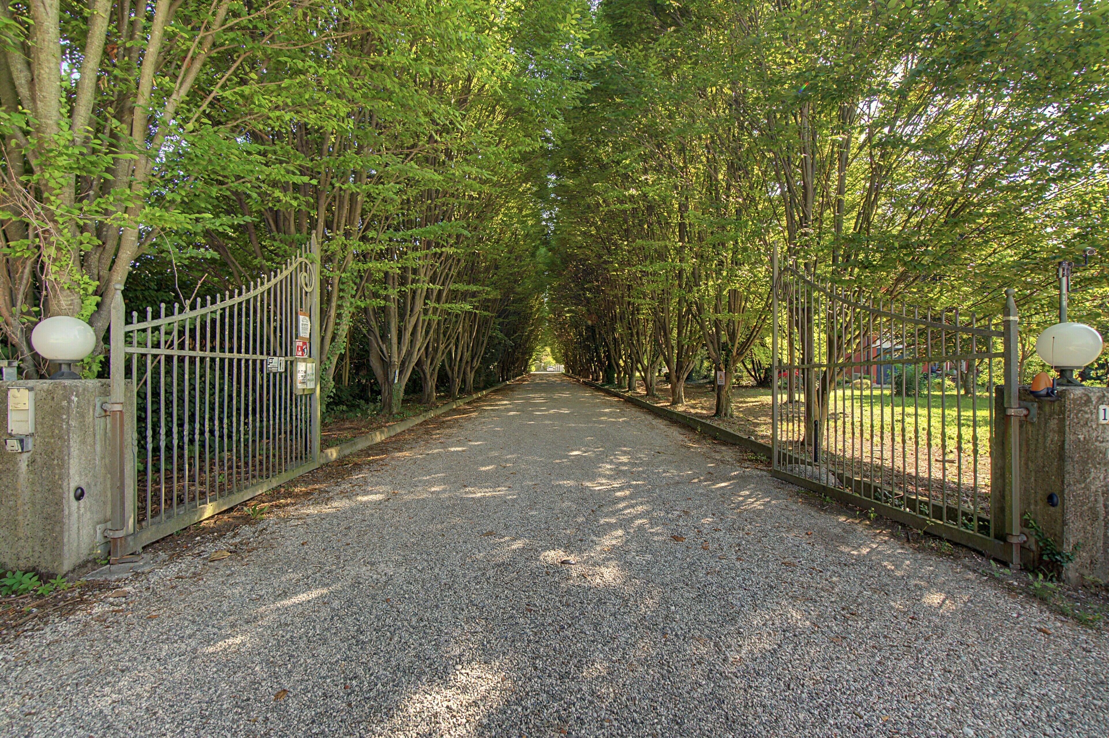 Un camino de grava bordeado por vallas de metal y árboles, que conduce a una zona cerrada.
