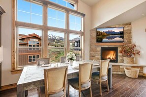 Un comedor con un ventanal grande, una chimenea y un televisor montado en la pared.