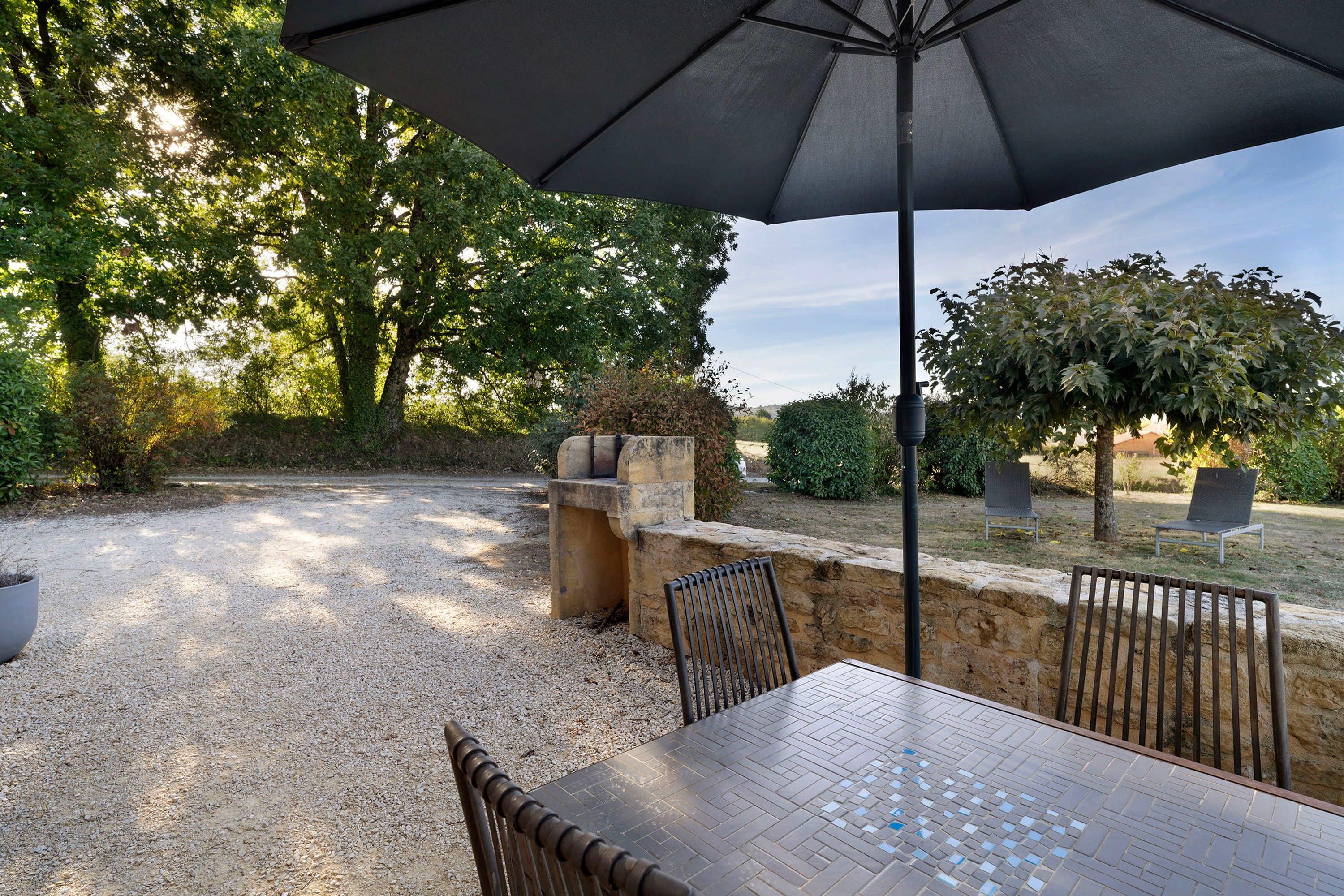 Patio esterno con tavolo e sedie, circondato da alberi e un muro in pietra.