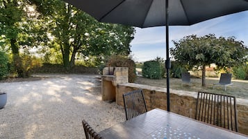Une terrasse extérieure avec une table et des chaises, entourée d’arbres et d’un mur de pierres.