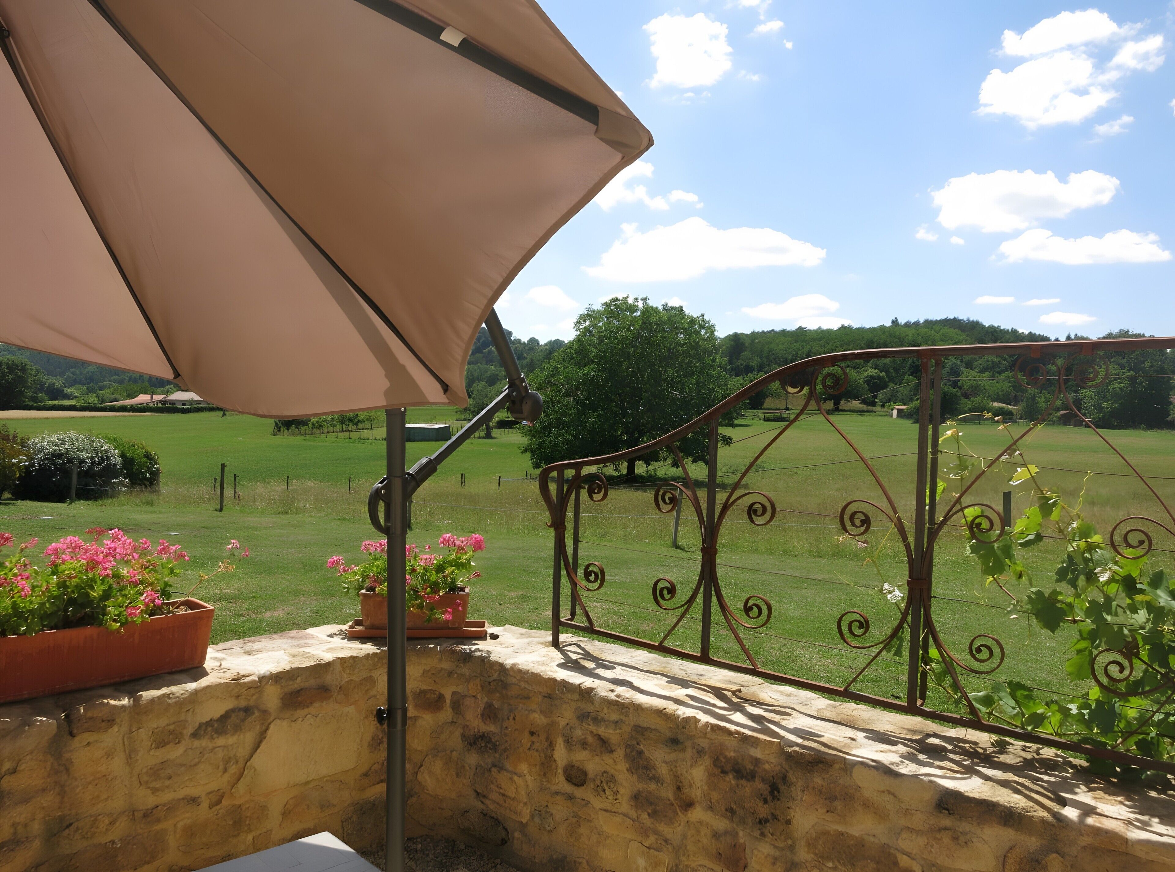 Un balcon donnant sur un champ verdoyant, avec une rambarde en métal et un parasol beige.