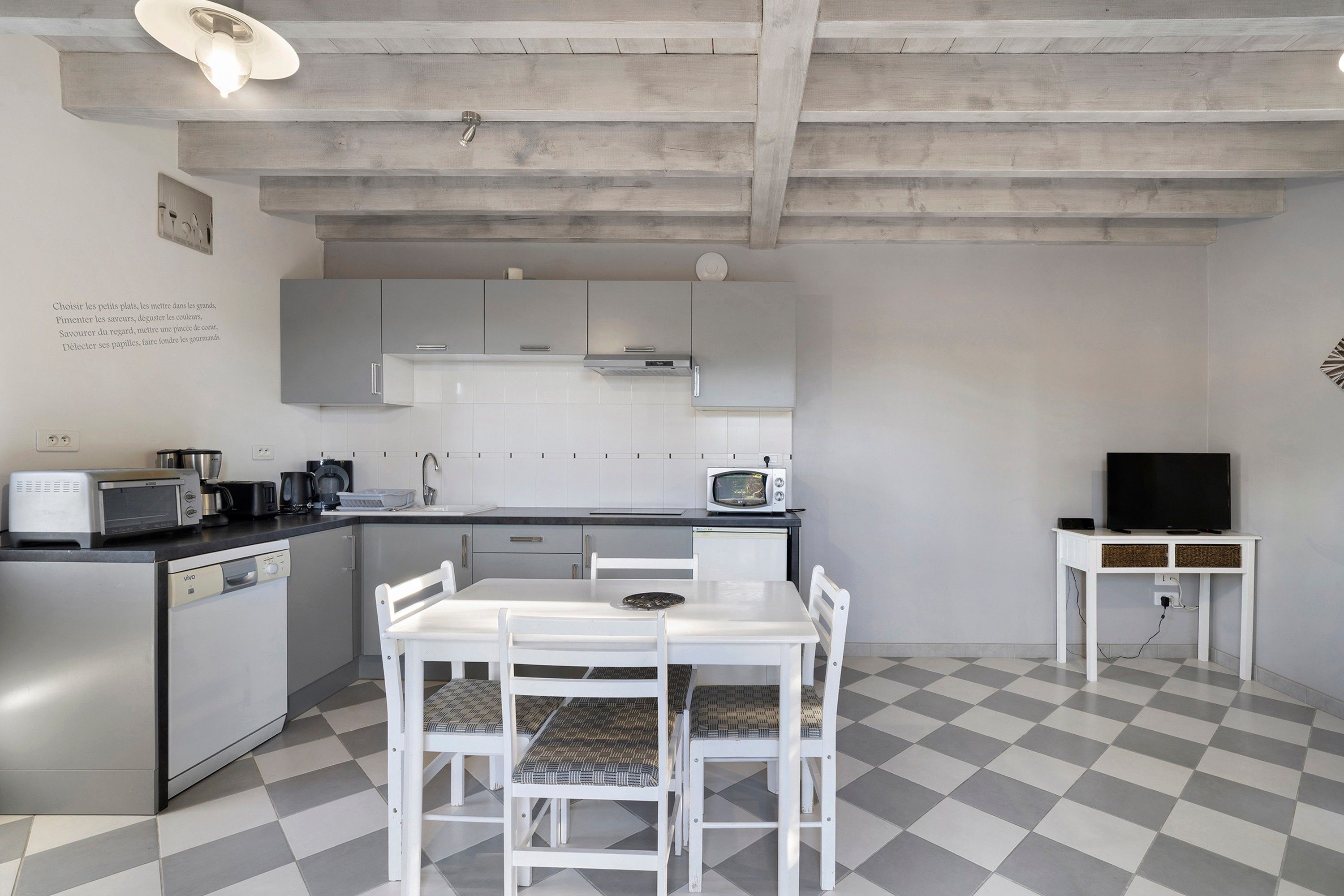 Een compacte keuken met witte kastjes, een eettafel met stoelen, een magnetron en een televisie op een meubel.