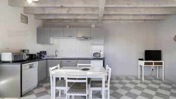 Een compacte keuken met witte kastjes, een eettafel met stoelen, een magnetron en een televisie op een meubel.