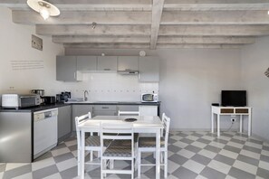 Une cuisine compacte avec des meubles blancs, une table à manger avec des chaises, un four à micro-ondes et un téléviseur posé sur un meuble.
