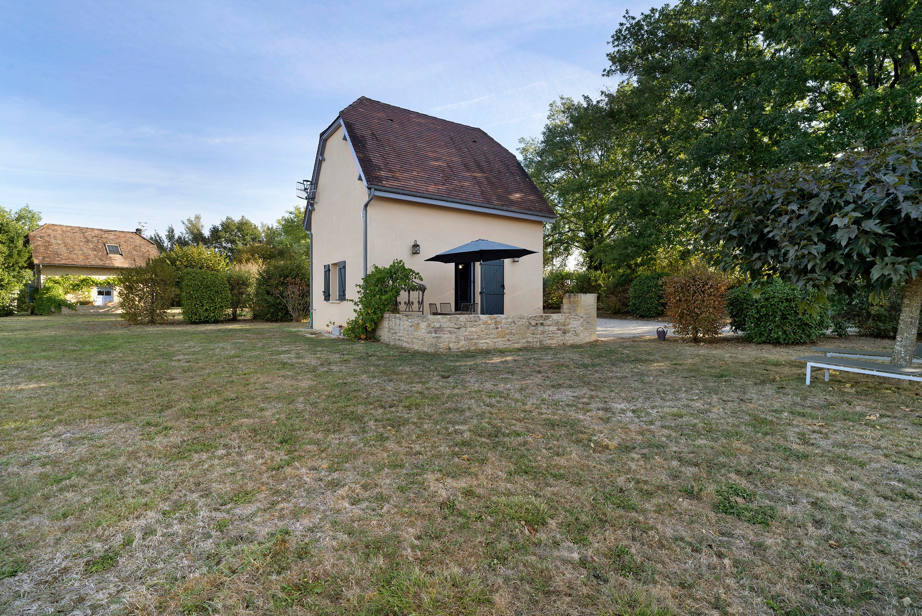 A single-story house with a sloped roof, a stone foundation, and a small patio area with a table and chairs.