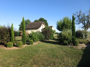 Una casa amb teulada inclinada, envoltada d'un jardí ben cuidat amb arbustos variats i gespa.