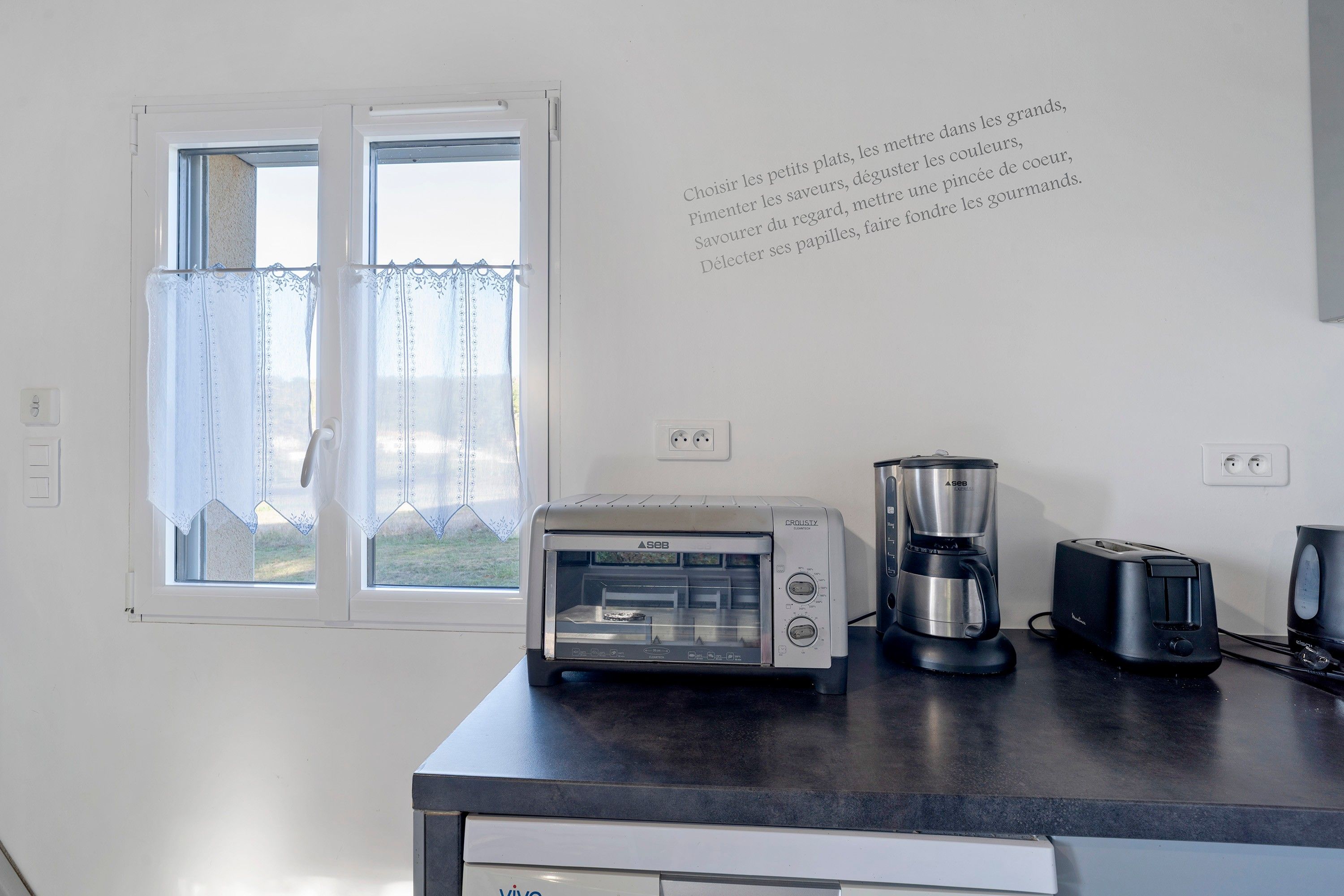 Een keuken met een broodrooster, koffiezetapparaat en een in de muur gemonteerde oven.