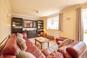 Een woonkamer met een bank, een houten salontafel, een boekenkast, een spiegel en een raam met gordijnen.