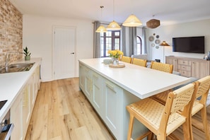 A modern kitchen with a large island, wooden chairs, pendant lights, and a flat-screen TV. - Host & Stay | Puffin Cove (Seahouses)