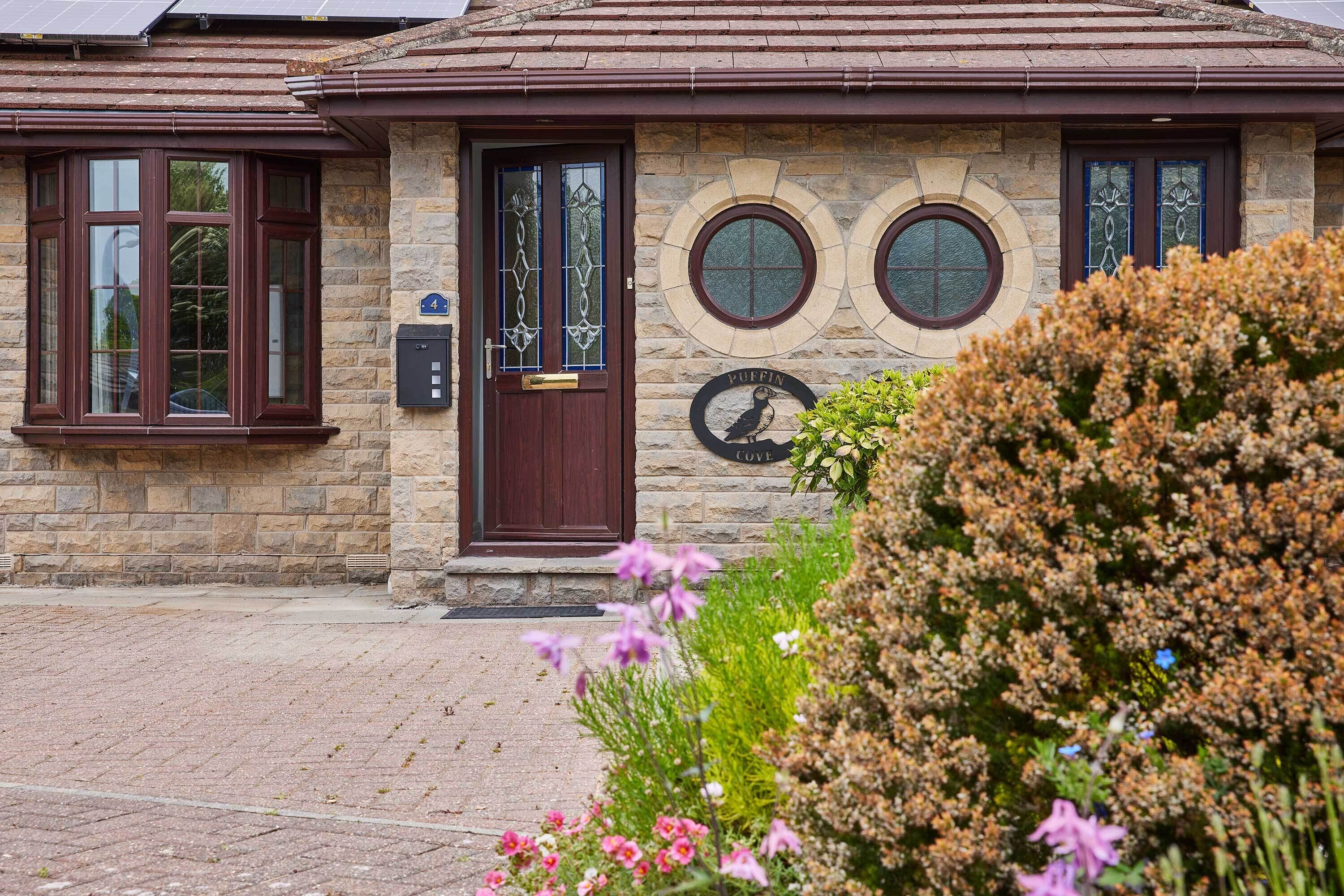 A stone building with a dark brown door, two round windows with a stone frame, and a sign with a bird and the word 'PUFFIN' on the wall.